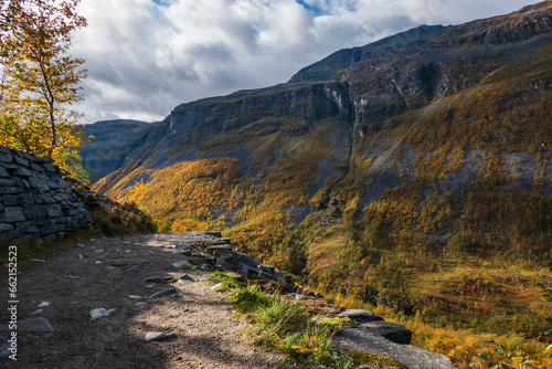 Rocky naturepath leading towards autumn colored steep mountain. Sunlight on mountain side. Norwegian nature.