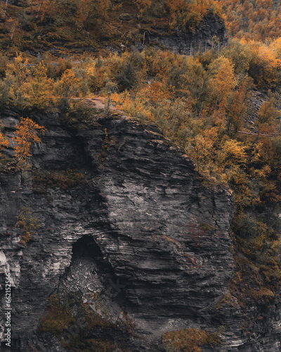 Mysterious cave entrance on the side of the cliff. Autumn colors on the trees. Norwegian nature.