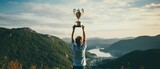 a boy holds a large cup aloft, symbolically on a high mountain overlooking the valley with river