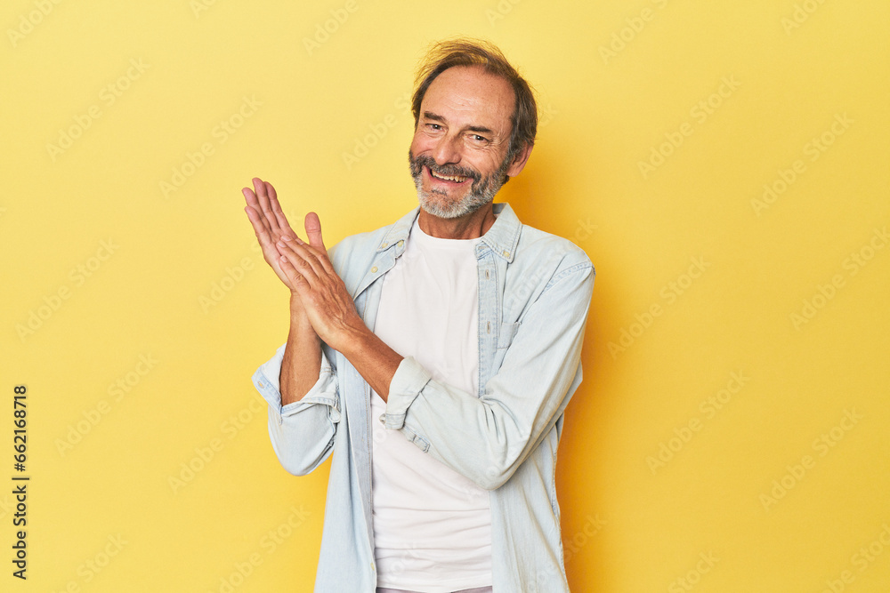 Caucasian middle-aged man in yellow studio feeling energetic and comfortable, rubbing hands confident. Caucasian middle-aged man in yellow studio feeling energetic and comfortable, rubbing hands confident.