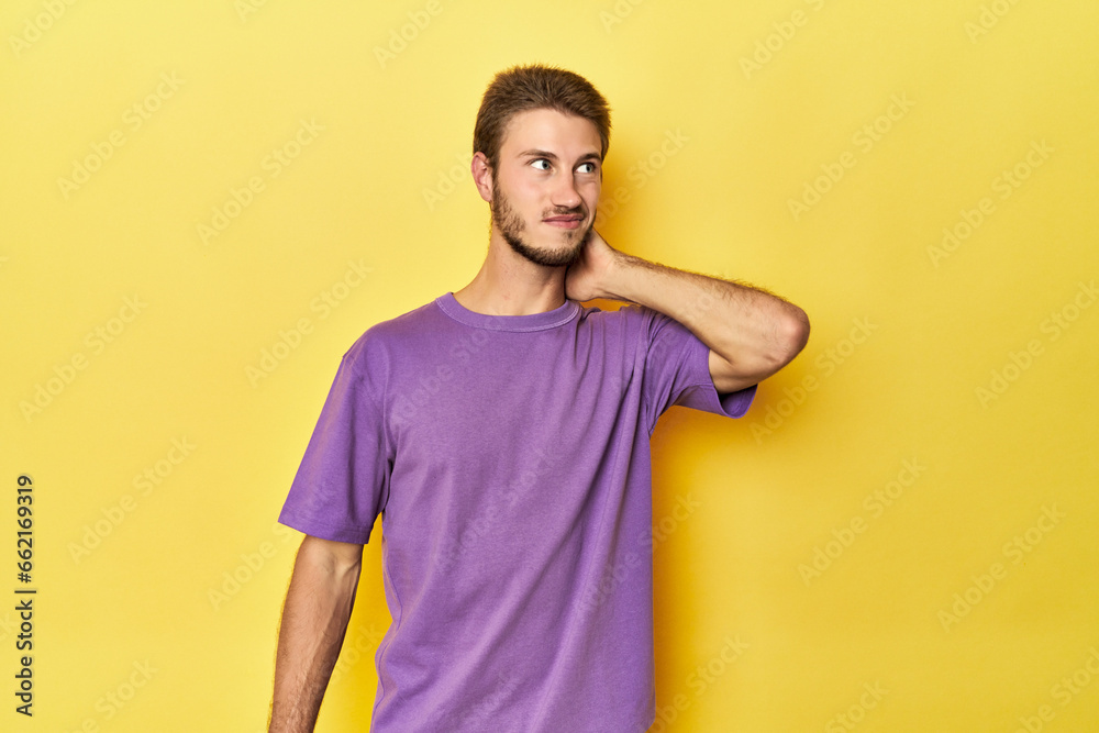 Young Caucasian man on a yellow studio background touching back of head, thinking and making a choice.