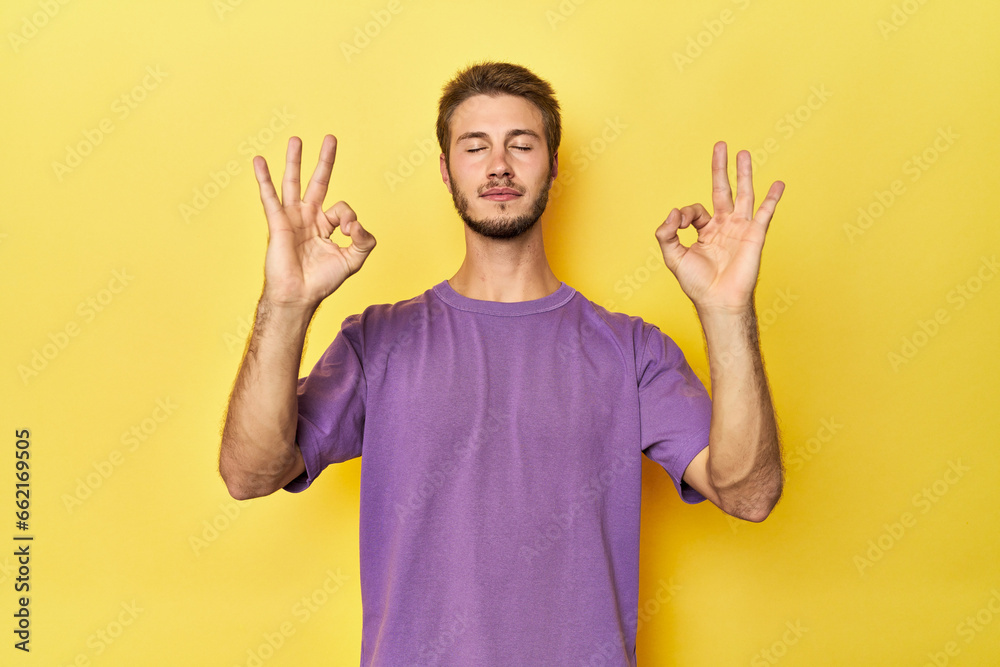 Young Caucasian man on a yellow studio background relaxes after hard working day, she is performing yoga. Young Caucasian man on a yellow studio background relaxes after hard working day, she is performing yoga.