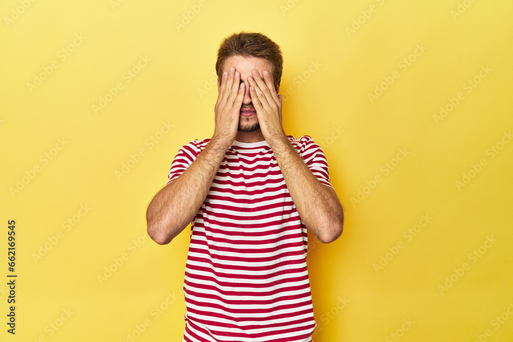 Young Caucasian man on a yellow studio background afraid covering eyes with hands. Young Caucasian man on a yellow studio background afraid covering eyes with hands.