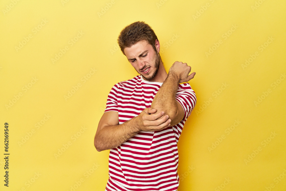 Young Caucasian man on a yellow studio background massaging elbow, suffering after a bad movement. Young Caucasian man on a yellow studio background massaging elbow, suffering after a bad movement.