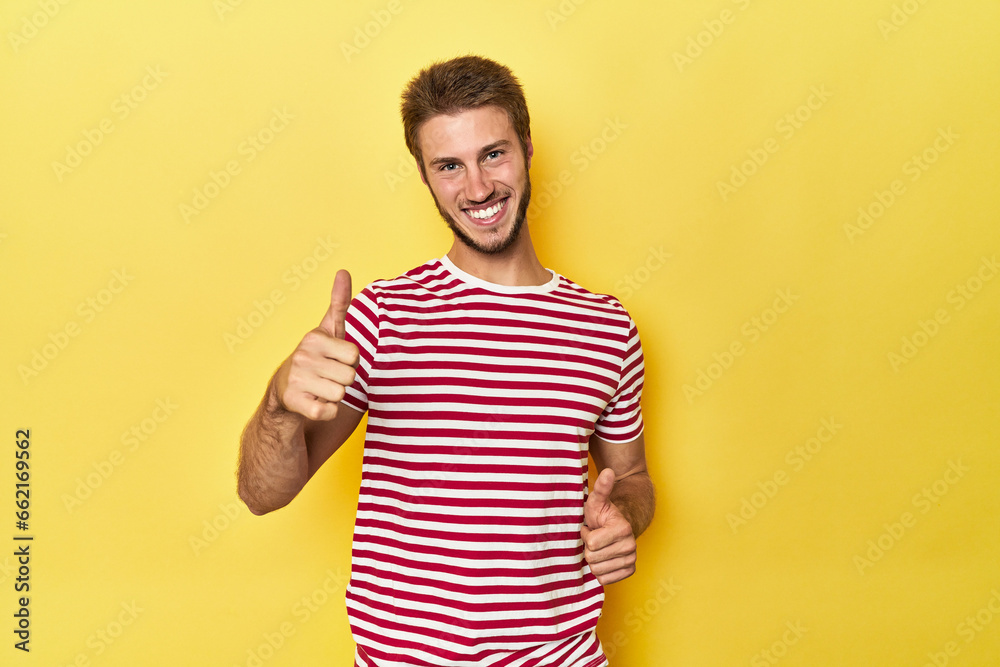 Young Caucasian man on a yellow studio background raising both thumbs up, smiling and confident. Young Caucasian man on a yellow studio background raising both thumbs up, smiling and confident.