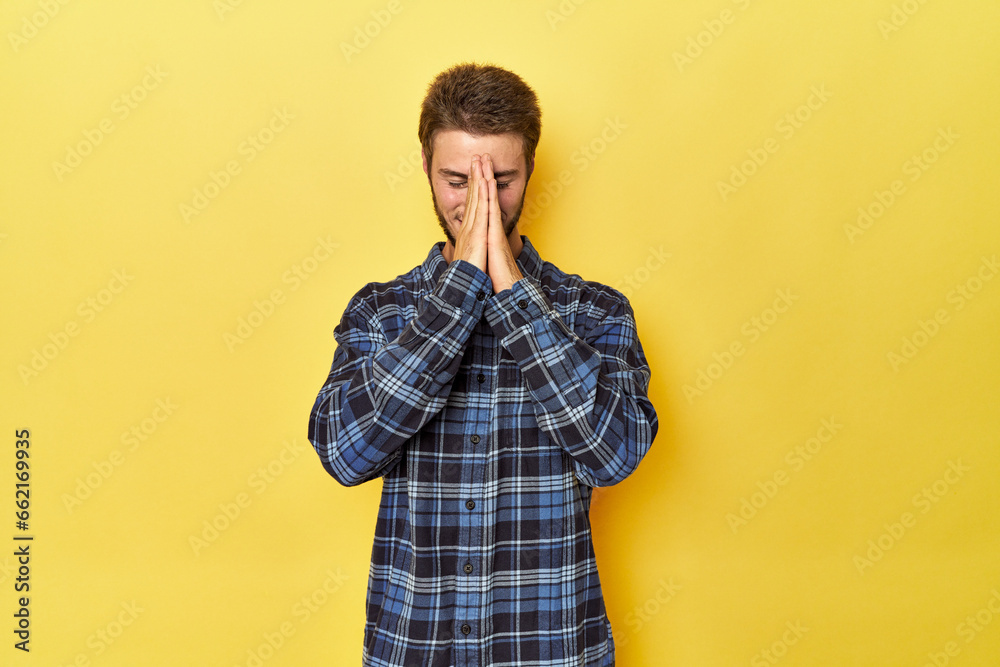 Young Caucasian man on a yellow studio background holding hands in pray near mouth, feels confident. Young Caucasian man on a yellow studio background holding hands in pray near mouth, feels confident.