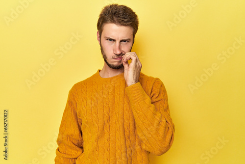 Young Caucasian man on a yellow studio background with fingers on lips keeping a secret. © Asier