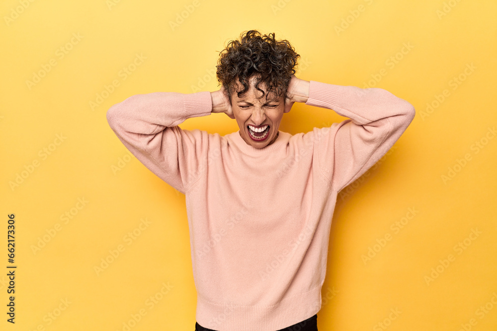 Mid-aged caucasian woman on vibrant yellow covering ears with hands trying not to hear too loud sound. Mid-aged caucasian woman on vibrant yellow covering ears with hands trying not to hear too loud sound.