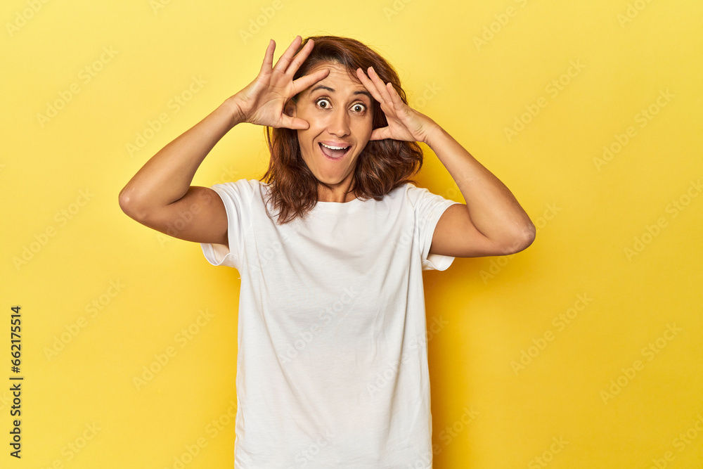 Middle-aged woman on a yellow backdrop keeping eyes opened to find a success opportunity. Middle-aged woman on a yellow backdrop keeping eyes opened to find a success opportunity.