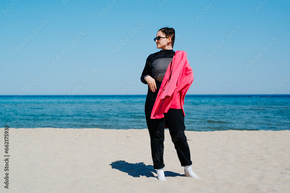 Young woman in casual clothes and pink jacket posing on the beach Young woman in casual clothes and pink jacket posing on the beach