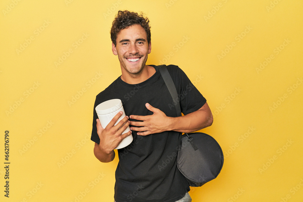Young Latino with protein bottle on yellow laughs out loudly keeping hand on chest. Young Latino with protein bottle on yellow laughs out loudly keeping hand on chest.