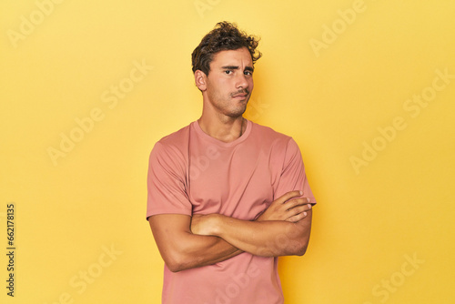 Young Latino man posing on yellow background suspicious, uncertain, examining you.