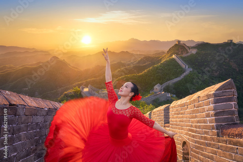 Chinese woman ballet dancer with red dress dancing at sunset in the Great Wall. Woman ballerina dance in ballerina shoes dancing with red silk gown flying on wind and the Great Wall at sunset. China photo