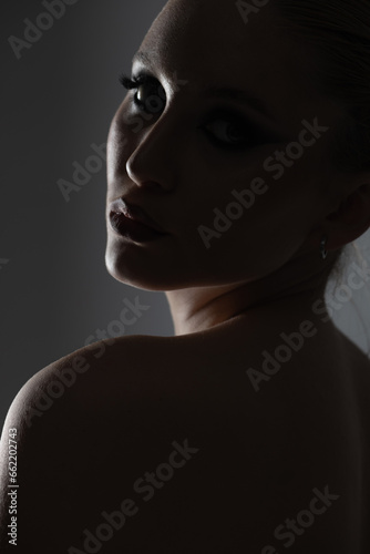 Beauty  fashion  style and make-up concept. Beautiful woman dark silhouette portrait. Model looking with seductive look through her shoulder. Studio shot on gray background