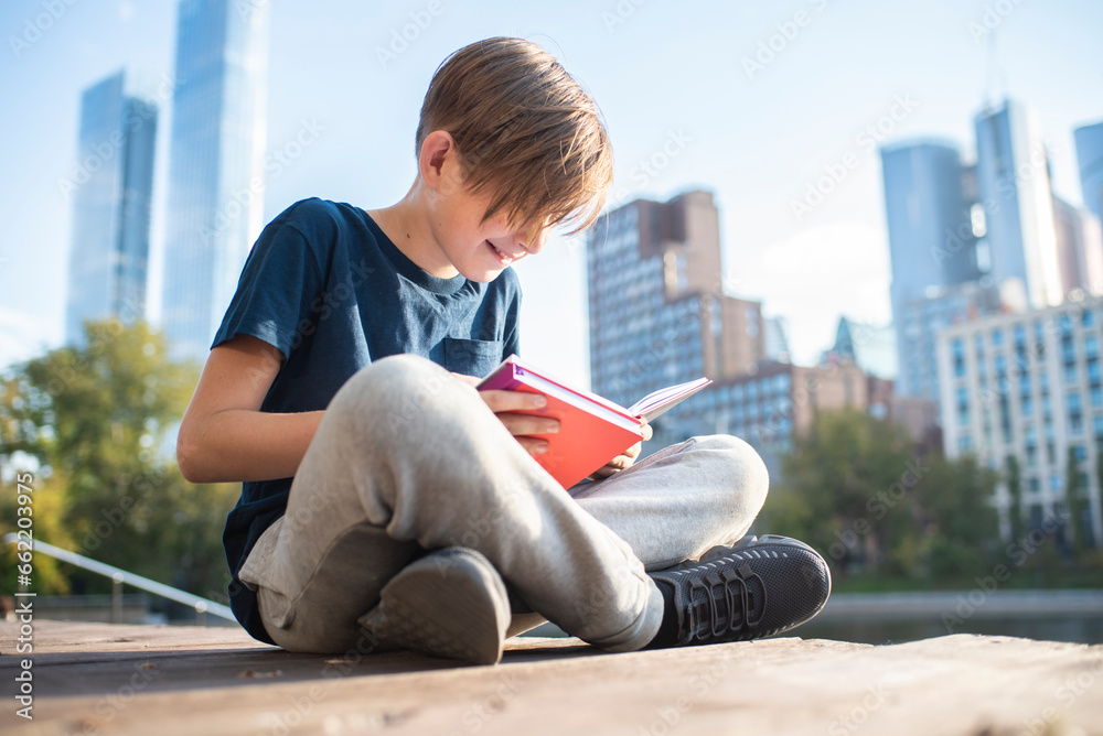 happy teenager reading a book in a metropolis park, against the backdrop of skyscrapers on a sunny day. Cute little boy reading a book sitting on a bench in the city