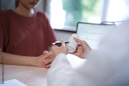 Asian psychologist women showing pills bottle to explaining medicine and prescription to female patient while giving counseling to explaining about mental health therapy to female patient in clinic