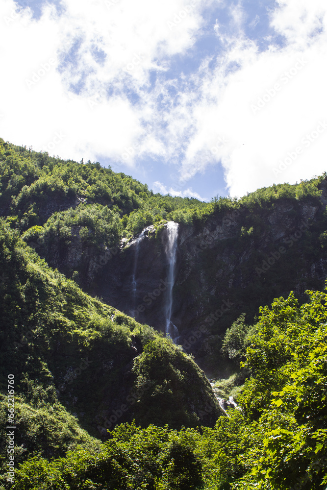 Beautiful polikara waterfall among green trees in Krasnaya polyana russia on a sunny summer day and a space for copying