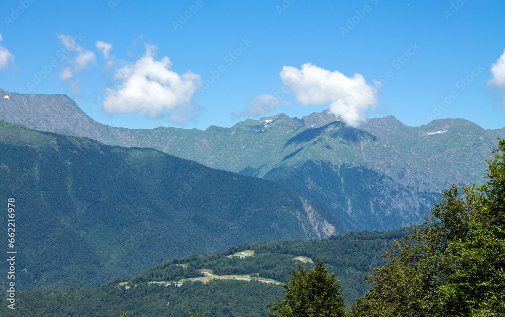 green mountain slopes and white clouds against a blue clear sky on a sunny summer day and a space for copying in krasnaya polyana