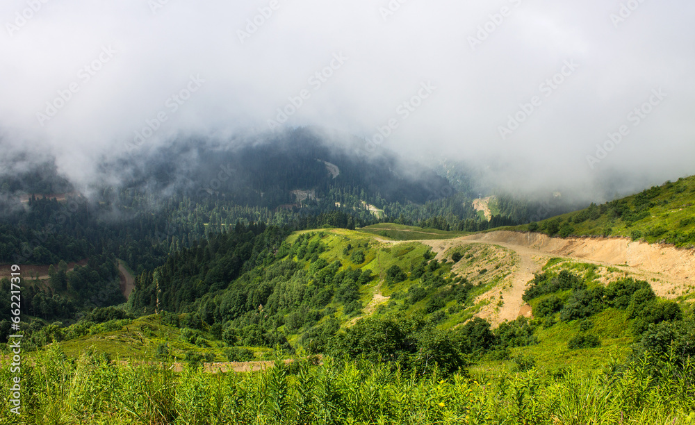 Fototapeta premium A beautiful dramatic landscape - green hillsides and mountains among white clouds and a space to copy on a summer day in Krasnaya Polyana in Russia