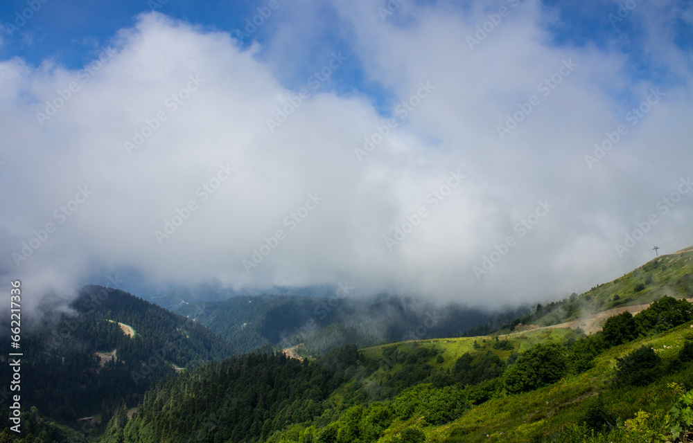 A beautiful dramatic landscape - green hillsides and mountains among white clouds and a space to copy on a summer day in Krasnaya Polyana in Russia