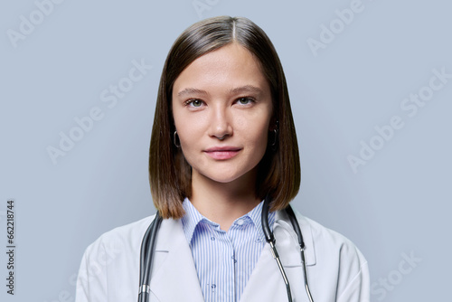 Headshot portrait of young friendly female medical worker on gray background