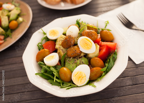 Dish of fresh vegetables arugula, avocado, cherry tomatoes with olives and quail eggs on dining table