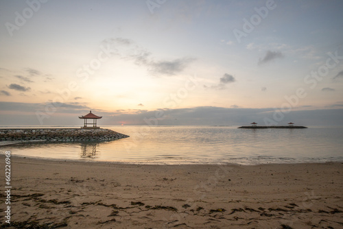 Magical sunrise with clouds in the sky. Dramatic sky at Sanur beach, Denpasar in Bali. Temple in the calm sea in the morning. Tropical landscape shot