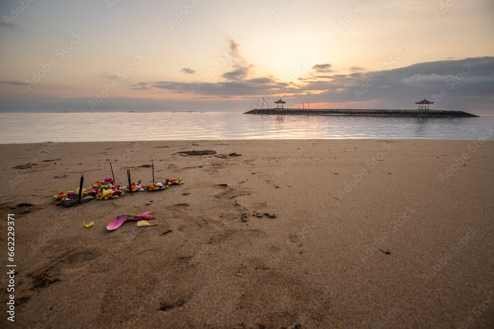Sunrise at the sandy beach of Sanur. Temple in the water. Offerings by the sea on the beach. Hindu faith in Sanur on Bali. Dream island and dream destination