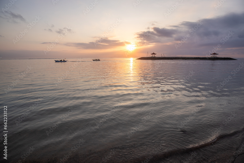 Sunrise at the sandy beach of Sanur. Temple in the water. Traditional fishing boat, Jukung on the beach. Hindu faith in Sanur on Bali. Dream island and dream destination