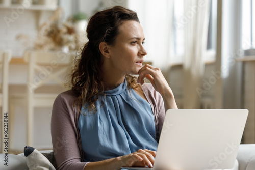 Pensive millennial remote employee woman distracting from work at laptop, looking away with thoughtful face, touching chin, thinking of startup project, future career vision, planning business tasks