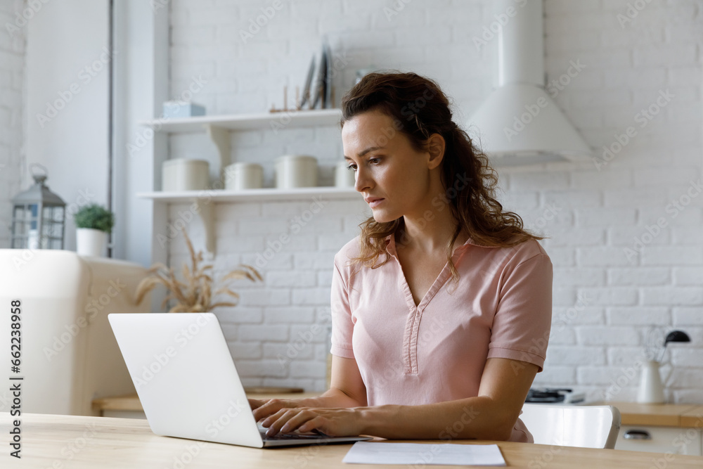 Focused serious freelancer woman using computer in kitchen. Remote employee working on online project from home office, typing on laptop, writing article, chatting with customers Focused serious freelancer woman using computer in kitchen. Remote employee working on online project from home office, typing on laptop, writing article, chatting with customers