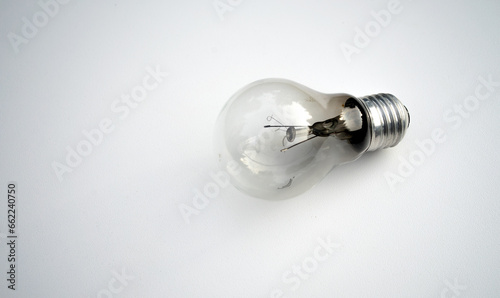 A glass burnt-out incandescent lamp on a white table.An old lighting lamp with a burnt-out spiral.