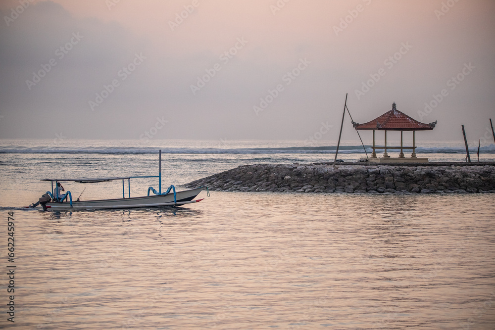 Sunrise at the sandy beach of Sanur. Temple in the water. Traditional fishing boat, Jukung on the beach. Hindu faith in Sanur on Bali. Dream island and dream destination
