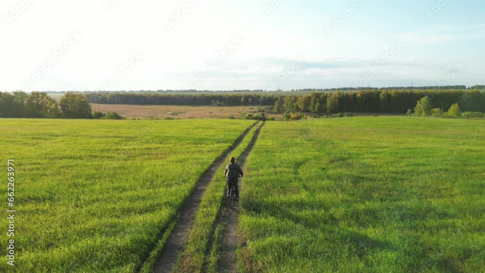Aerial view of a man cycling along a country road and grassy field. The man rides a bicycle in the meadow. Aerial view of a man cycling along a country road and grassy field. The man rides a bicycle in the meadow.