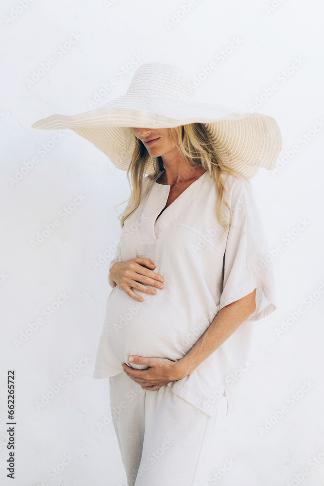 Young beautiful pregnant woman in white clothes and a large tropical hat. Young beautiful pregnant woman in white clothes and a large tropical hat.