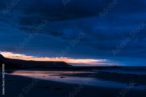 Beautiful sunrise landscape image of Kennack Sands in Cornwall UK wuth dramatic moody clouds and vibrant sunburst