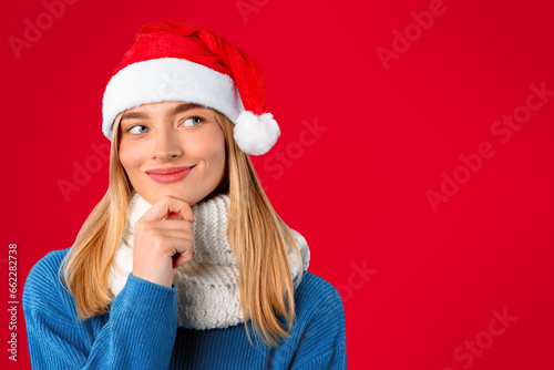 Dreamy woman in Santa hat looking at copy space and touching chin over red background  banner