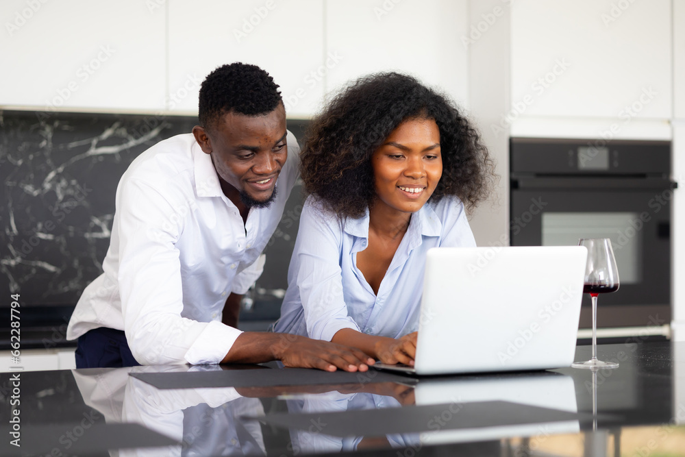 Couple using laptop computer in kitchen at home. Happy excited successful African American man and woman couple togetherness at home office. Work from home Couple using laptop computer in kitchen at home. Happy excited successful African American man and woman couple togetherness at home office. Work from home