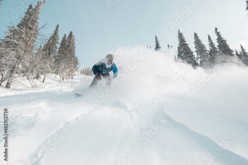 Male snowboarder riding in snow on sunny day. Snowy slope with beautiful mountain valley view