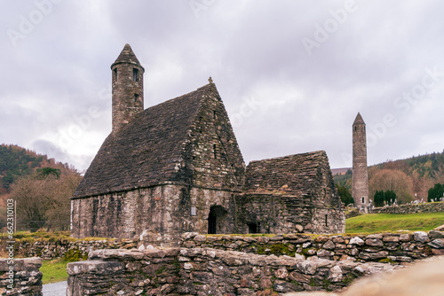 Old brick building with round tower and cloudy sky at churchyard in Glendalough's monastic town. Early medieval monastic settlement founded by St Kevin in the 6th century