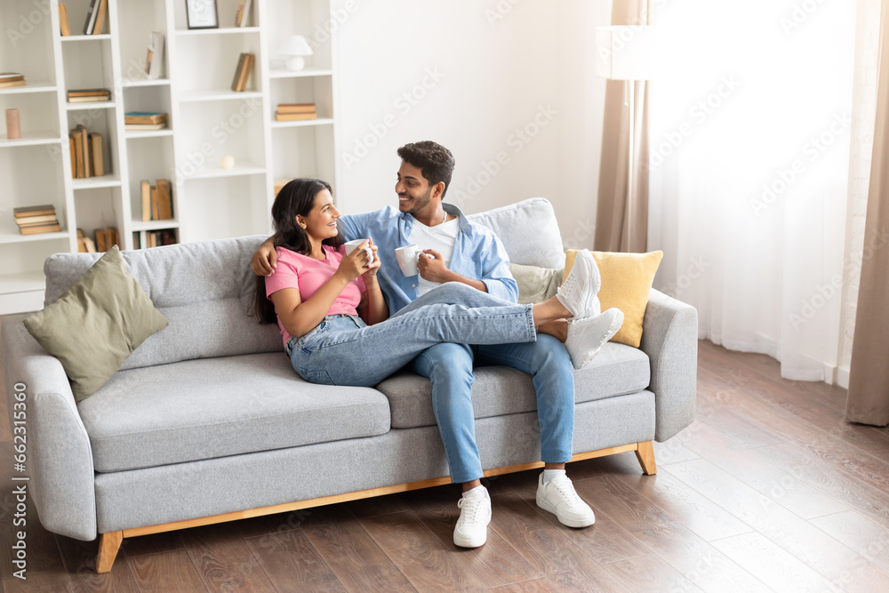 Smiling young indian couple drinking coffee and chatting on couch