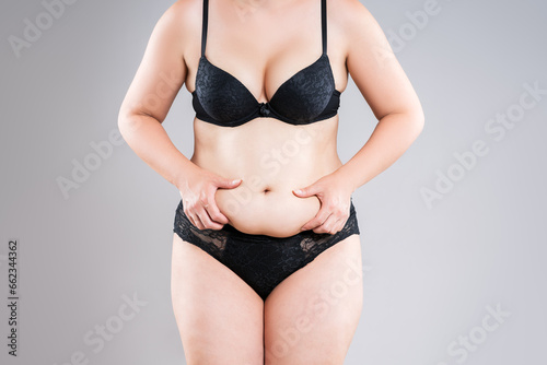 Tummy tuck, flabby skin on a fat belly, fat woman in black lingerie, plastic surgery concept on gray background