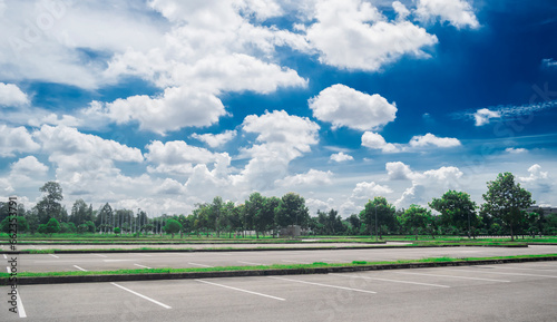 Wide empty asphalt parking lot background with white painted lines marked lens. Outdoor empty space parking lot with trees and cloudy sky. outside parking lot in a park