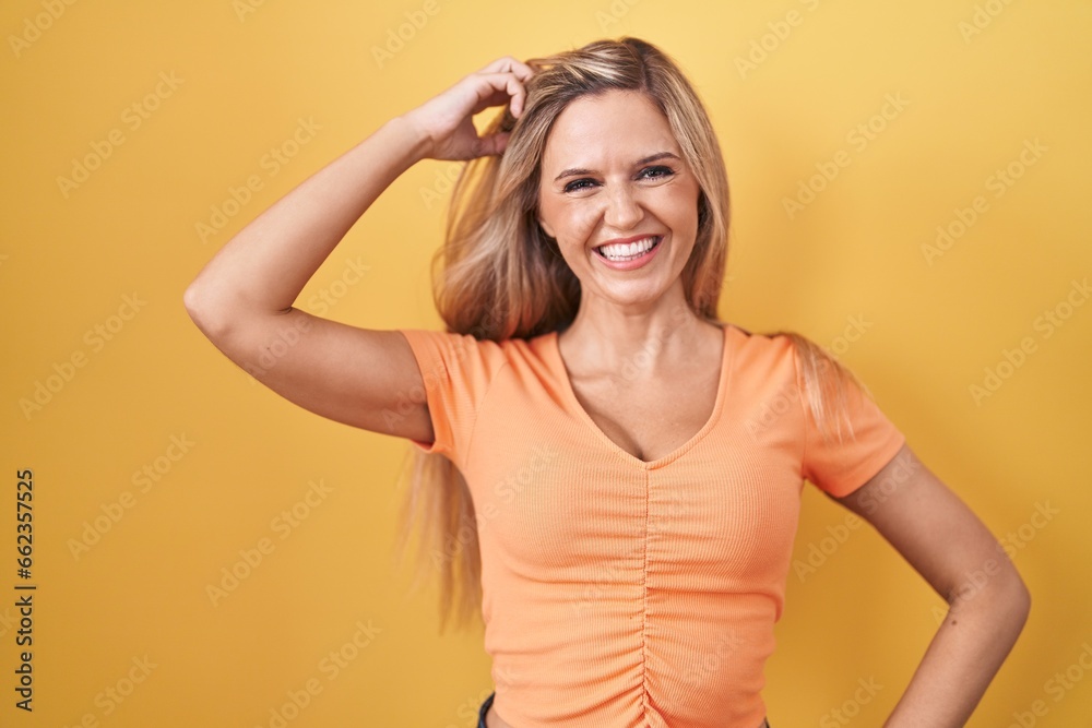 Young woman standing over yellow background smiling confident touching hair with hand up gesture, posing attractive and fashionable Young woman standing over yellow background smiling confident touching hair with hand up gesture, posing attractive and fashionable