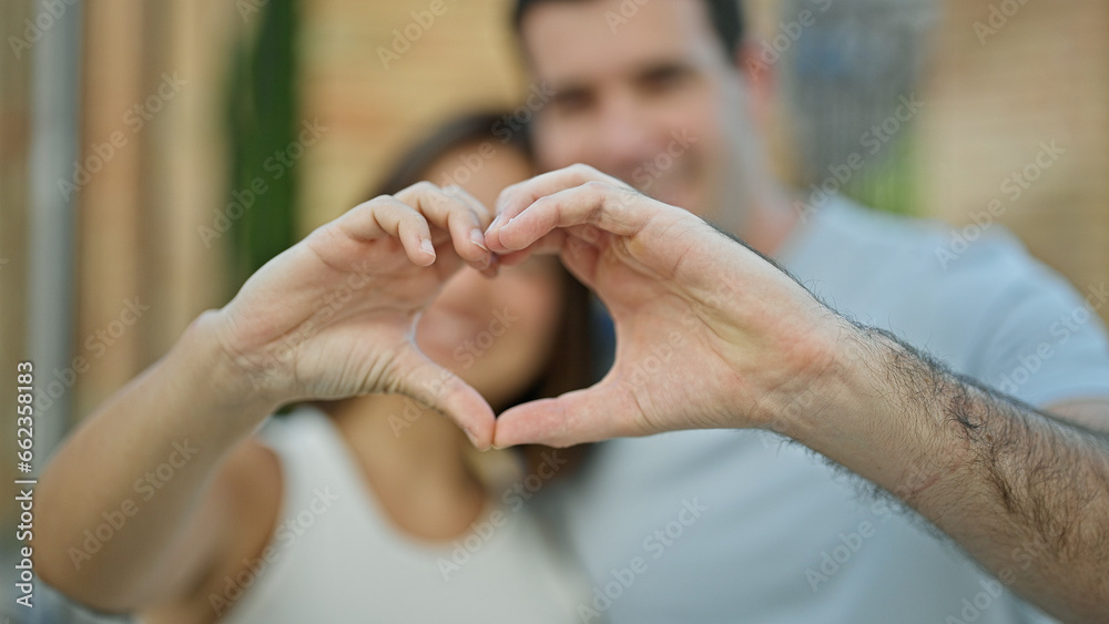 Fototapeta premium Beautiful couple smiling confident doing heart gesture with hands at street