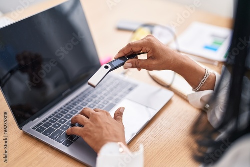 Middle age hispanic woman using laptop holding portable memory at office