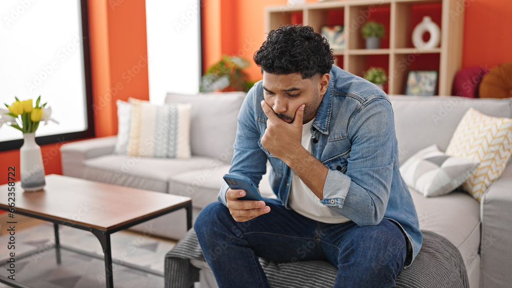 African american man using smartphone with worried expression at home