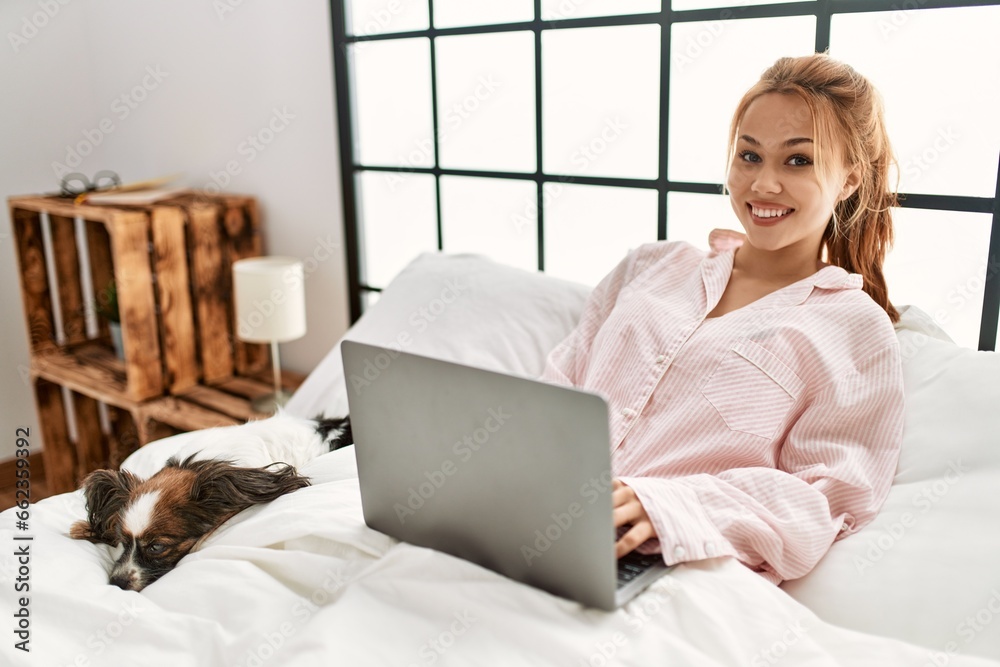 Young caucasian woman using laptop sitting on bed with dog at bedroom Young caucasian woman using laptop sitting on bed with dog at bedroom