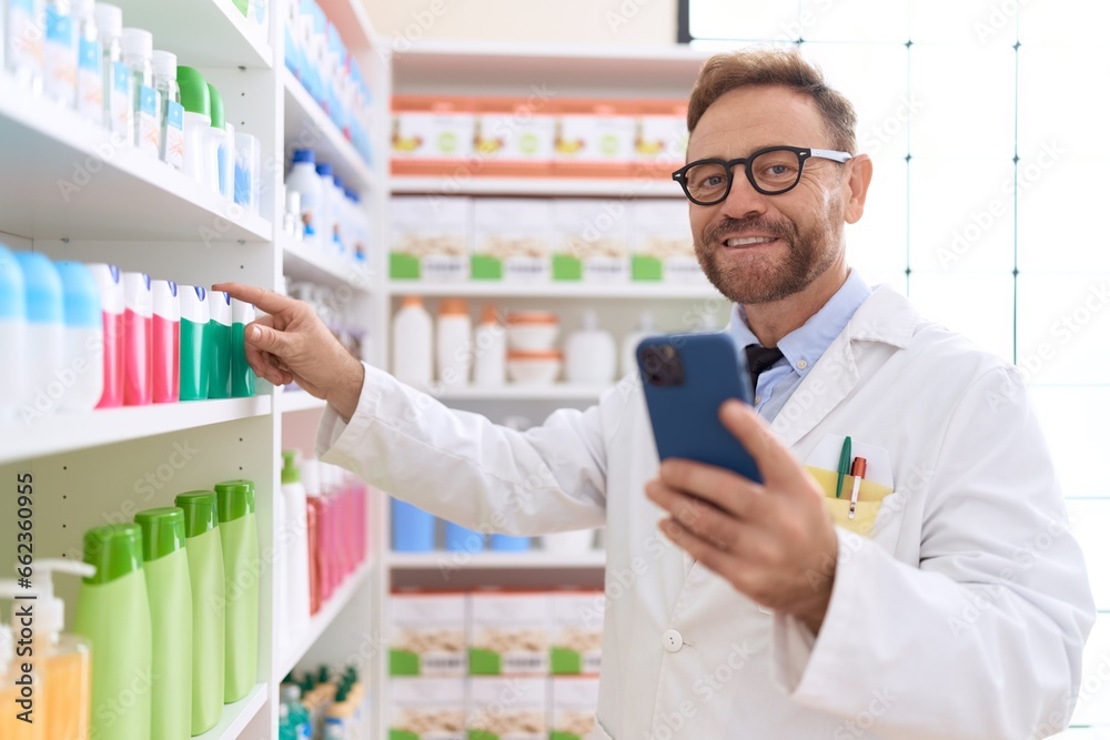 Middle age man pharmacist using smartphone working at pharmacy Middle age man pharmacist using smartphone working at pharmacy