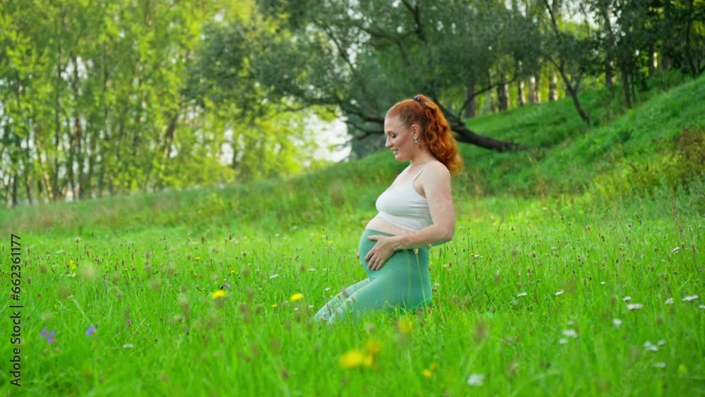 Redhead woman stroking pregnant tummy outdoors. Young expecting mother holding baby in pregnant belly and looking at camera. Concept of mother and child health. 4K, UHD Redhead woman stroking pregnant tummy outdoors. Young expecting mother holding baby in pregnant belly and looking at camera. Concept of mother and child health. 4K, UHD